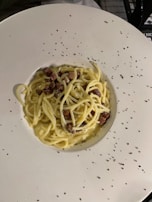A rustic bowl of spaghetti carbonara topped with crispy pancetta and a sprinkle of parmesan.
