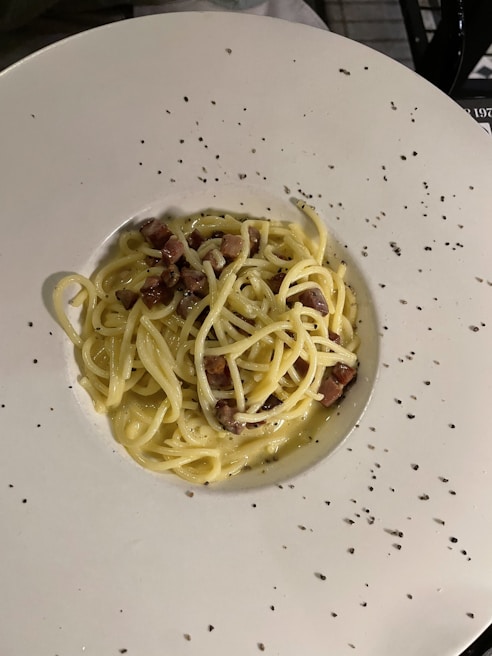 A colorful plate of spaghetti carbonara topped with crispy pancetta and a sprinkle of parmesan