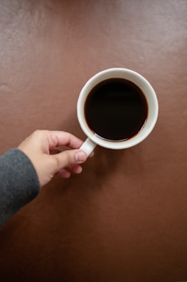 Hands holding a warm coffee cup over a cozy, textured fabric background.
