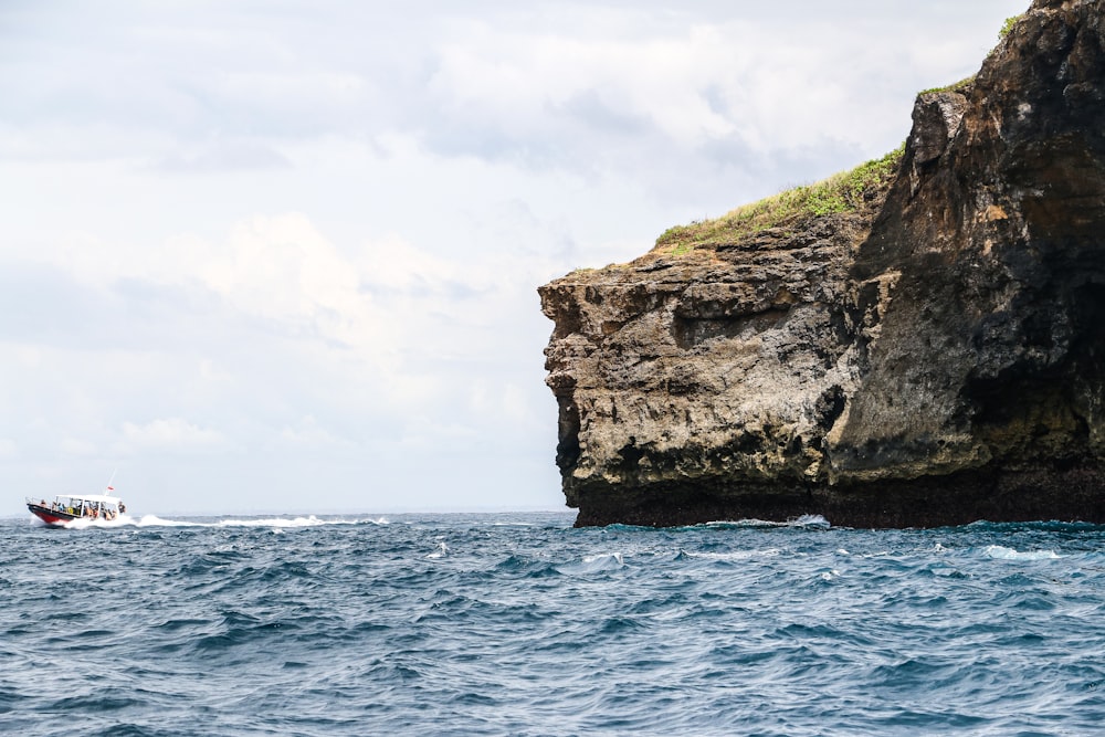 a boat traveling past a large rock formation in the ocean