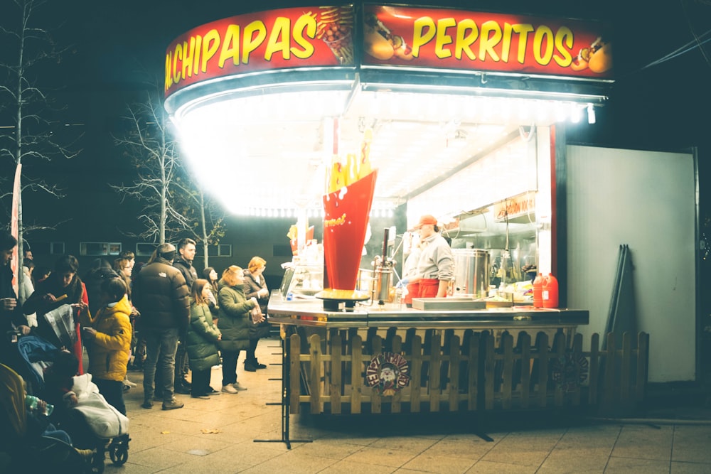 a group of people standing outside of a food stand