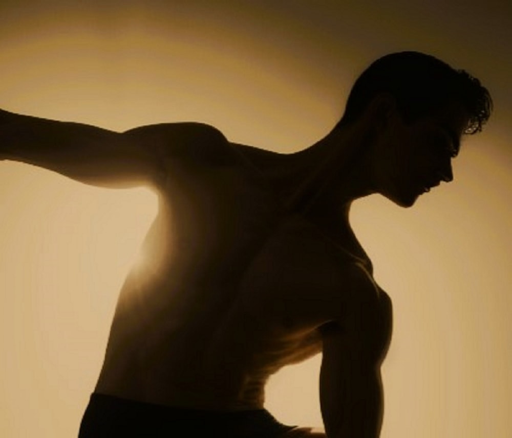 a shirtless man holding a skateboard in his right hand