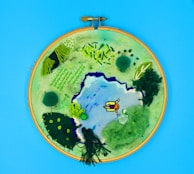 A vibrant textile artwork showing a landscape stitched with delicate thread details.