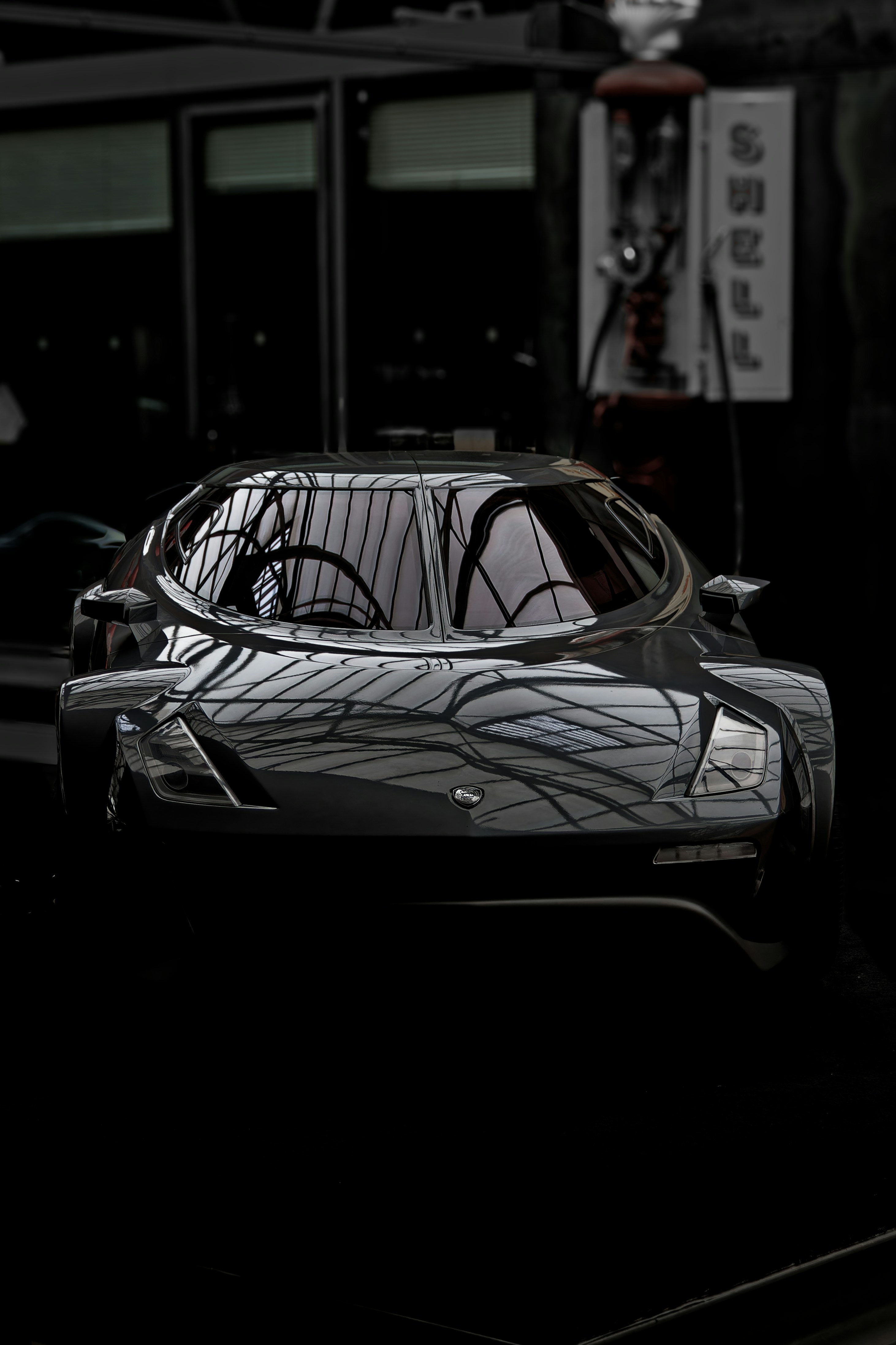 A sleek, modern car with a dark, reflective surface parked indoors. The lighting creates an intricate pattern on the car, highlighting its aerodynamic features. The setting appears to be a showroom or a garage with dim lighting.