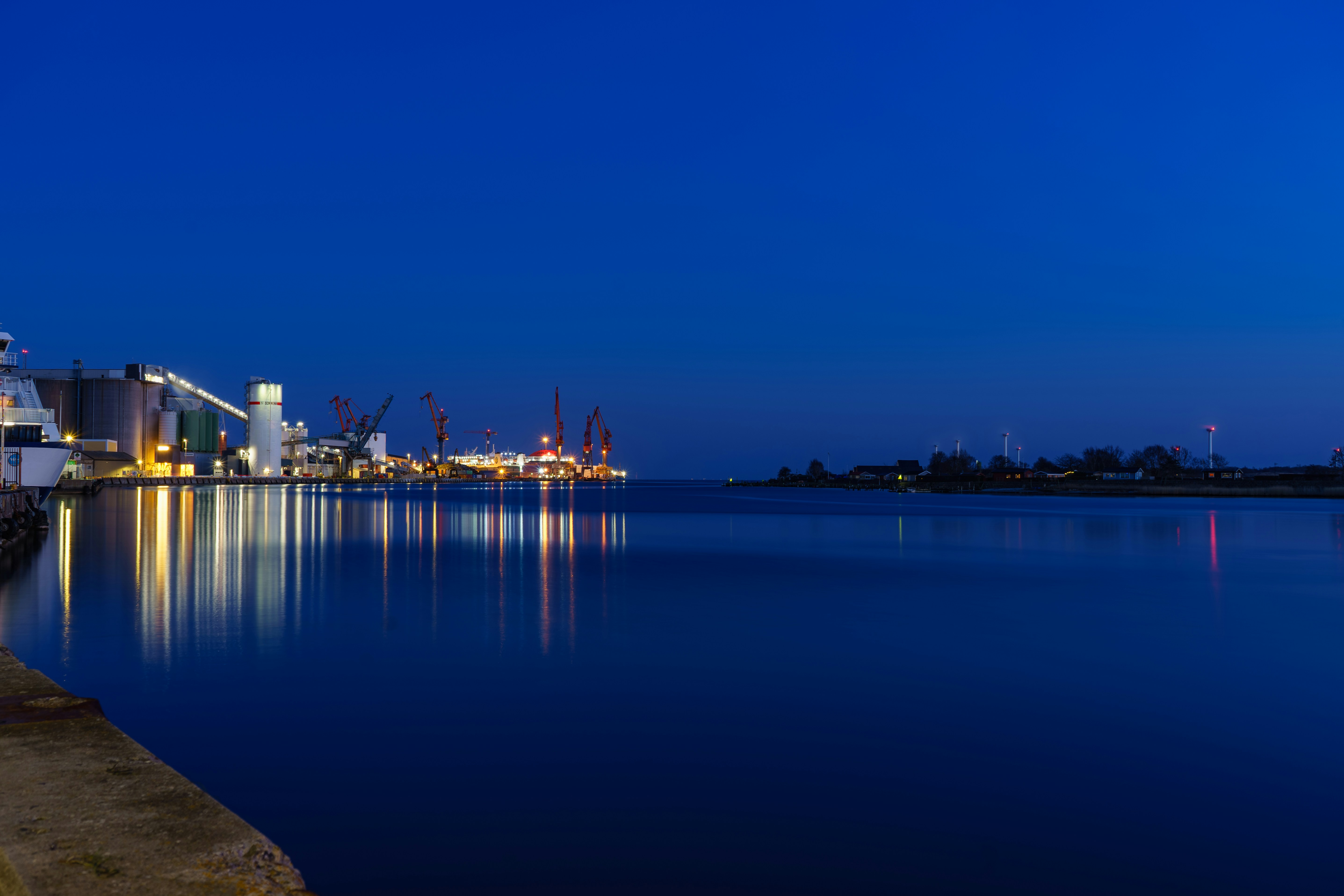 Cargo ship at port at dusk, deep blue sky, industrial logistics environment, dark water reflections