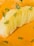 A stack of thinly sliced potatoes is artfully arranged and garnished with small sprigs of green herbs. The potatoes are placed against a backdrop of smooth, creamy orange sauce, with pieces of chopped green onions scattered around.