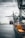 A large cargo ship is docked at an industrial port with towering cranes. Shipping containers are stacked on the ship and along the dock. The sky is overcast, creating a muted ambiance over the water.
