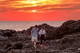 A couple walking hand in hand along a rocky coastline at golden hour.
