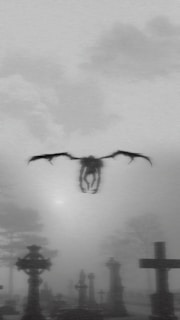 A dark, winged creature is flying over a foggy graveyard filled with crosses and tombstones. The atmosphere appears eerie and ominous, with minimal visibility due to the thick fog. Gloomy, overcast skies add to the overall mysterious ambiance.