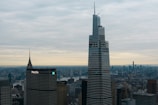 A cityscape featuring tall skyscrapers with modern architecture, set against a cloudy sky. The foreground displays prominent buildings with the MetLife building recognizable by its logo.