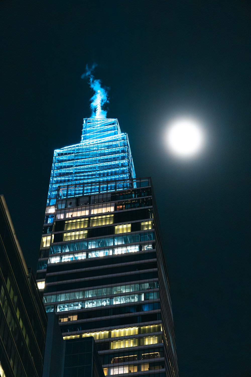 a tall building lit up at night with a full moon in the background