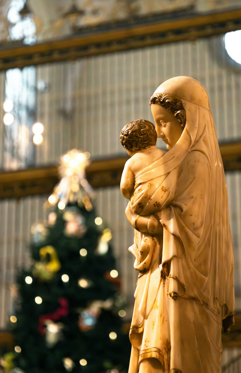 Uma estátua de uma mãe e filho em frente a uma árvore de Natal