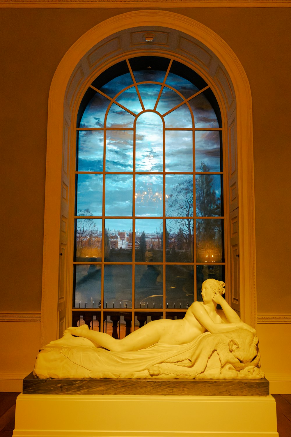 a statue of a woman laying down in front of a window