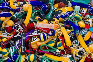 A colorful assortment of keychains featuring small sneaker and basketball designs, with various branding labels. The items are densely packed, displaying a mix of shapes and vibrant colors such as yellow, green, blue, red, and black.