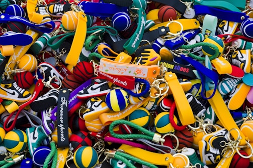 A colorful assortment of keychains featuring small sneaker and basketball designs, with various branding labels. The items are densely packed, displaying a mix of shapes and vibrant colors such as yellow, green, blue, red, and black.