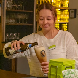 Friendly bartender pouring a cold beer in a lively cervecería setting.