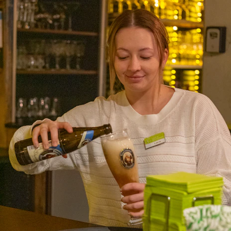 Cinematic shot of a bartender pouring craft beer with a warm, welcoming smile in a terracotta-colored setting.