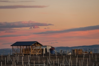 A warm Texas hill country sunset behind a sturdy steel-framed barndominium under construction.