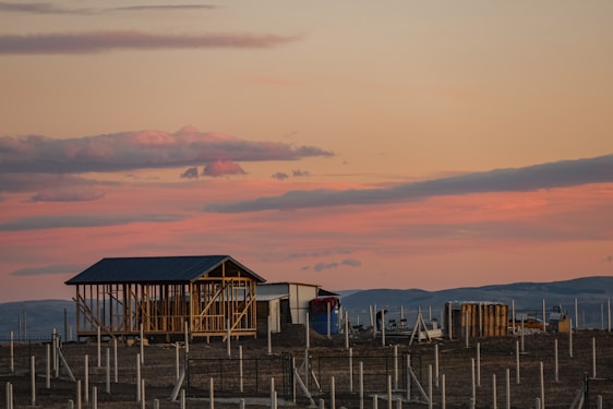 A warm Texas hill country sunset behind a sturdy steel-framed barndominium under construction.