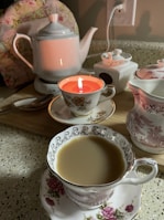 A cozy tea setup with a steaming teapot and delicate cups surrounded by flowers.