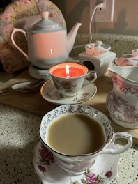 An elegant setup featuring raysleaf white tea in a glass teacup beside a gold-accented teapot with soft green leaves in the background.