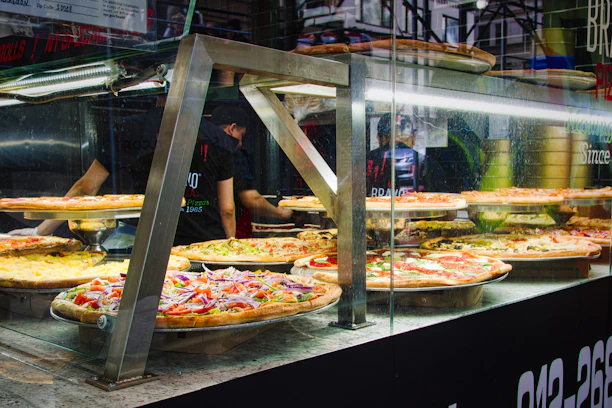 A warm, inviting buffet line filled with various New York-style pizza slices and fresh toppings.