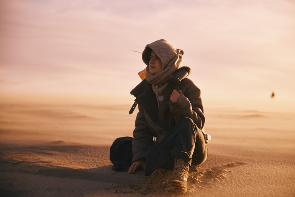 a person sitting in the sand with a hat on