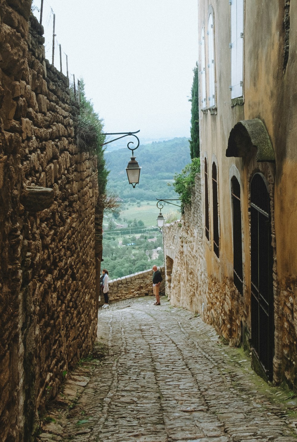 two people are walking down a cobblestone street