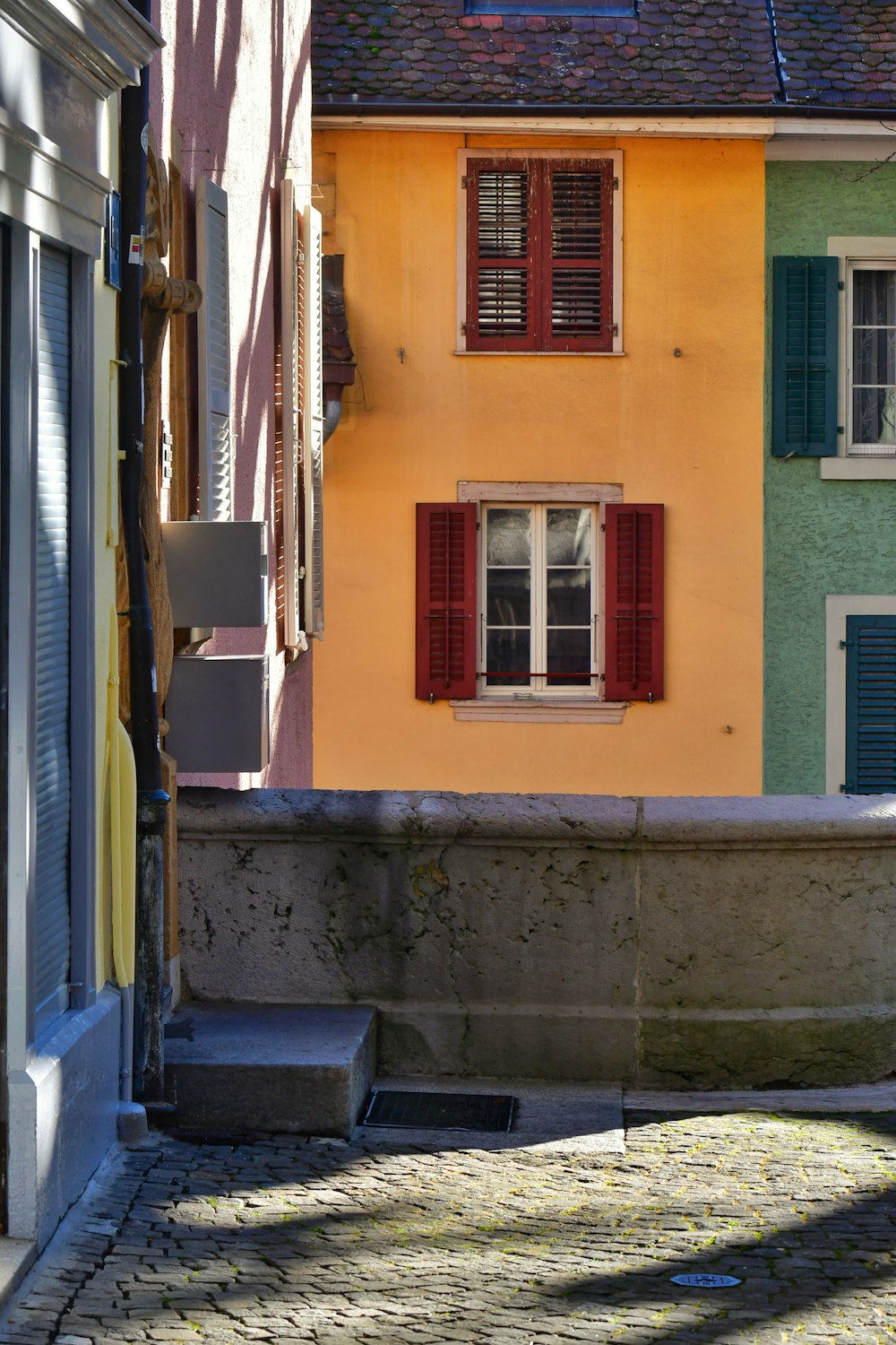 a yellow building with red shutters next to a green building