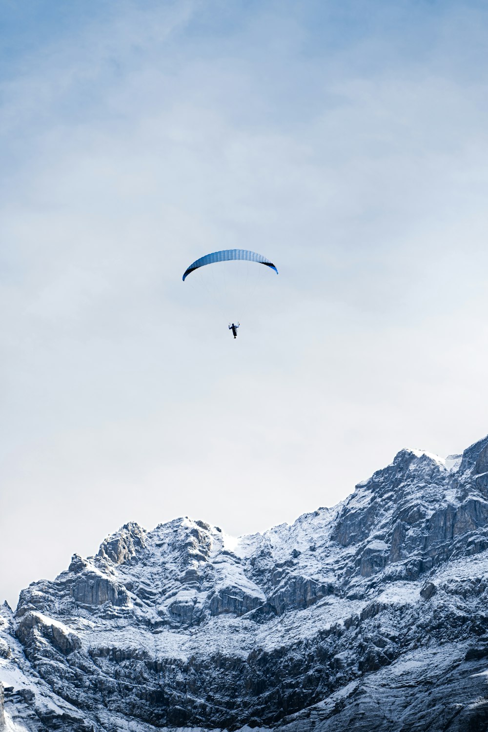 a paraglider flying over a snowy mountain range
