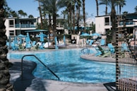 A sparkling resort pool surrounded by lounge chairs and palm trees under a clear blue sky.