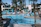 A relaxed couple lounging by the resort’s sparkling pool framed by palm trees under a clear blue sky.