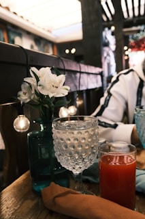 A close-up of a restaurant table with a sleek QR code stand next to a glass of water and a small vase of fresh flowers.