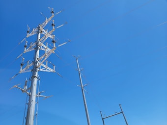 A tall metal structure with multiple crossbeams and insulators stands against a clear blue sky. Several power lines are connected to its top, extending across the image.