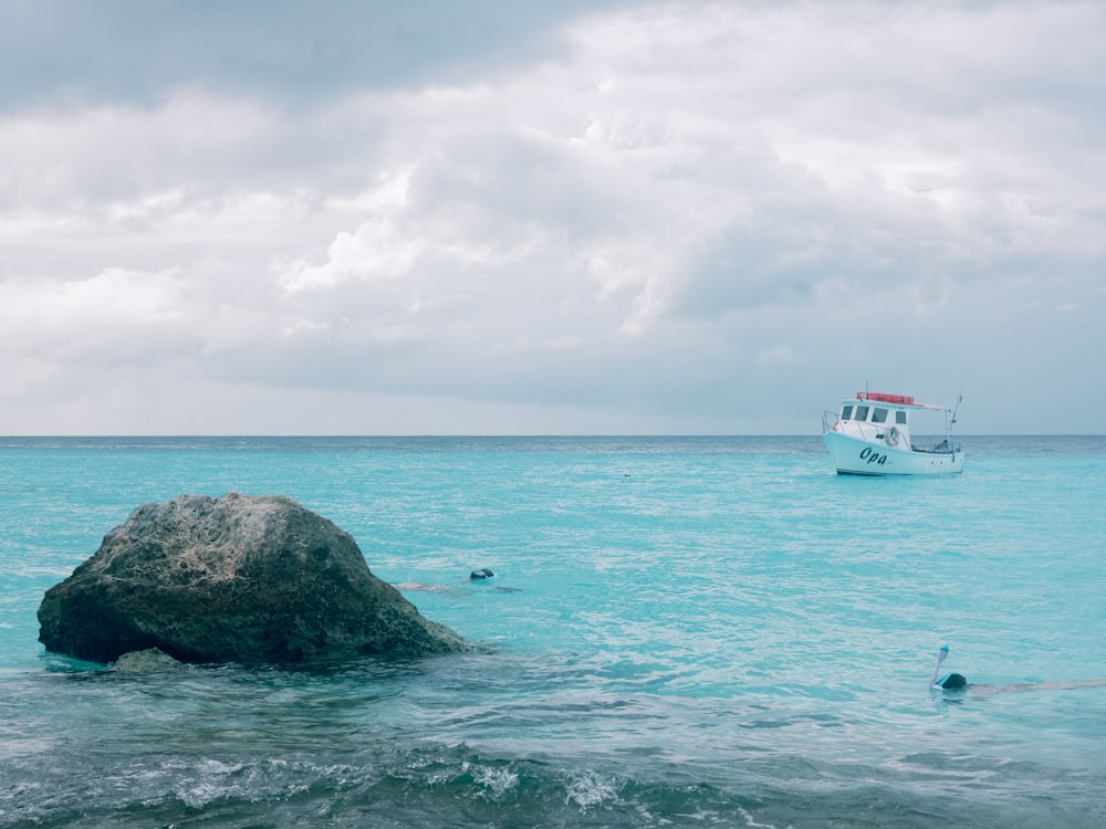 a boat in the ocean with a rock in the foreground