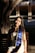A person is sitting on a wooden bench under a tree, wearing a blue and yellow graduation sash that reads 'UC Irvine'. The background features architectural elements and is partially shaded.
