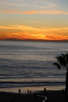 A vibrant sunset over a tropical beach with travelers enjoying the view.