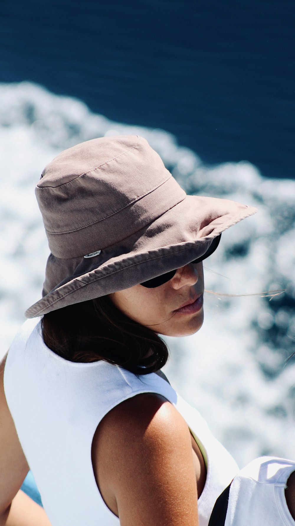 a woman wearing a hat standing next to a body of water