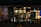 A nighttime view of a restaurant exterior with promotional posters on the windows offering deals such as 'Buy One Get One 50% Off' and 'Buy 4 Get 1 Free'. Interior lighting reveals menu boards displaying various food items.