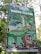 A promotional signboard for Curug Pletuk located in a lush, green area. The sign includes various offerings such as a camping package for the new year, starting December 2, 2023, to January 2, 2024. It features images of natural attractions, such as a waterfall and a pool, as well as local culinary highlights. The board details package prices and amenities like free parking and durian. Contact information and social media handles are visible at the bottom.