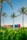 Colorful sign reading 'RIVIERA MAYA' stands under clear blue skies, surrounded by lush green foliage with tall palm trees in the background. The scene conveys a tropical beach vibe with a tranquil and inviting atmosphere.