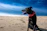 A happy dog wearing a seafoam green bandana sitting on sandy beach with ocean waves in the background.