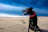 A happy dog wearing a seafoam green bandana sitting on sandy beach with ocean waves in the background.