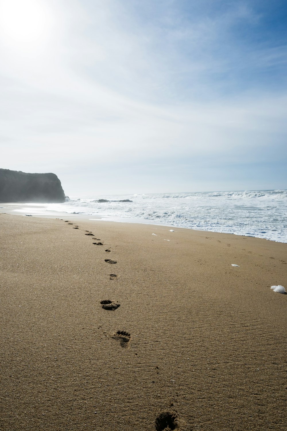 a beach with footprints in the sand and a cliff in the background