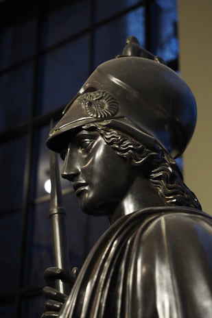 Close-up of a classical Greek warrior statue with intricate armor details against a dark background.