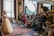 A bride in an elaborate wedding dress is posing, surrounded by a large group of photographers capturing her with professional cameras. The scene is set indoors, with natural light coming through large windows and additional lighting equipment in use.