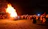 A joyful crowd dancing around a bonfire during the intercultural festival at sunset.