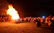 A joyful crowd dancing around a bonfire during the intercultural festival at sunset.