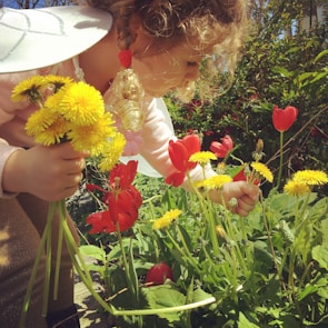 A child and mother planting flowers together in a sunny garden.