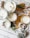 Several candles are arranged on a wooden surface, each in a glass container, with various decorations such as dried flowers, herbs, and pine cones around them. The setup includes autumn leaves and wooden beads, enhancing the rustic and cozy atmosphere.
